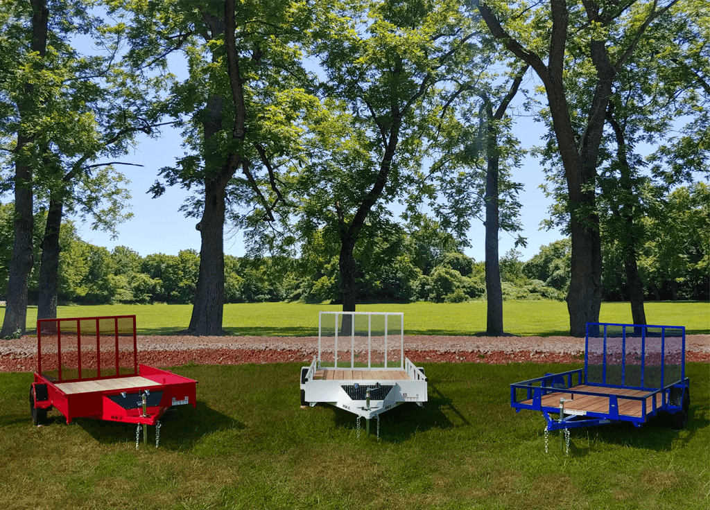 Three Rice Trailers one red, one white, and one blue in a field surrounded by trees.