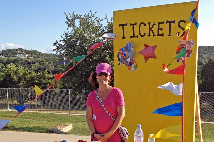 Image of a smiling carnival volunteer at a colorful ticket booth sign with pennants